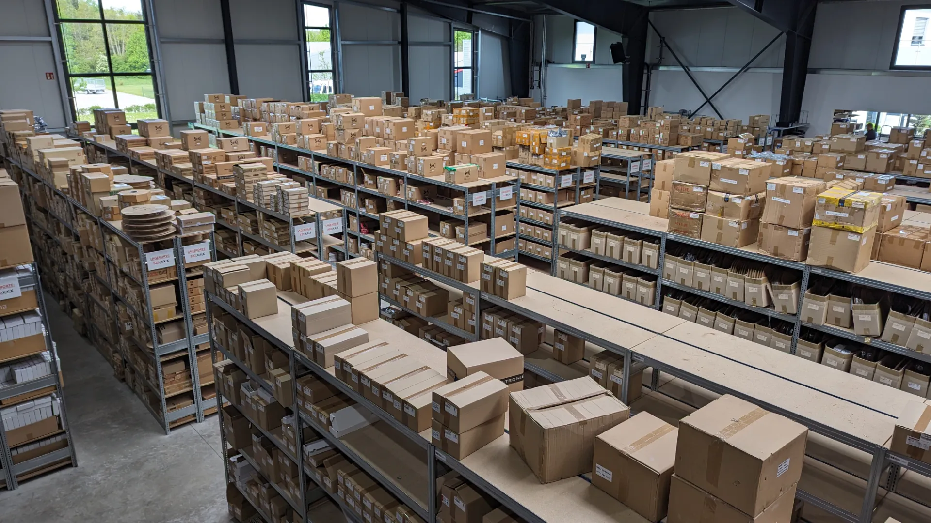 Aufgeräumtes Lager mit Regalen und Paletten voller Elektronik-Kartons – IT-Tronics Restposten Ankauf